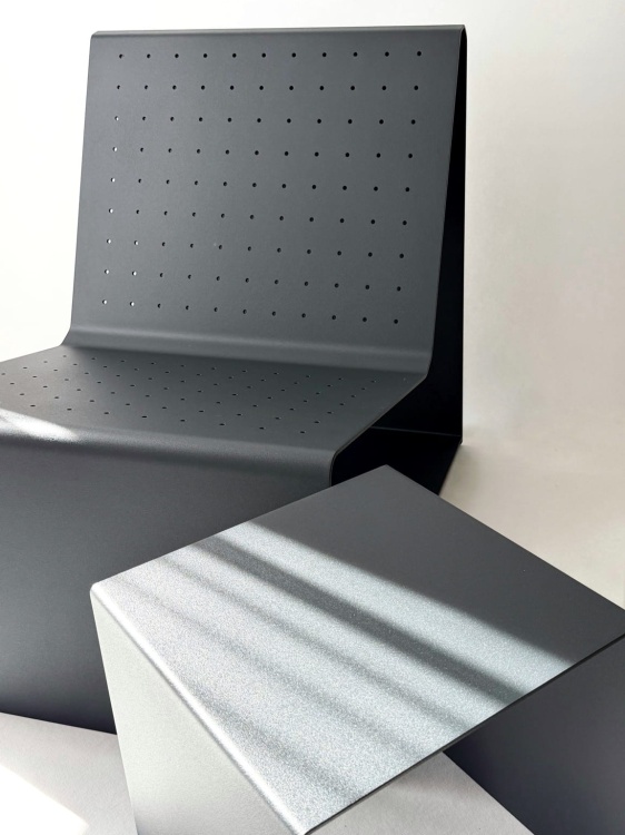 Perforowane oparcie filtruje światło, tworząc subtelny rytm cieni. Konstrukcja z aluminium zachowuje stabilność i lekkość wizualną.
